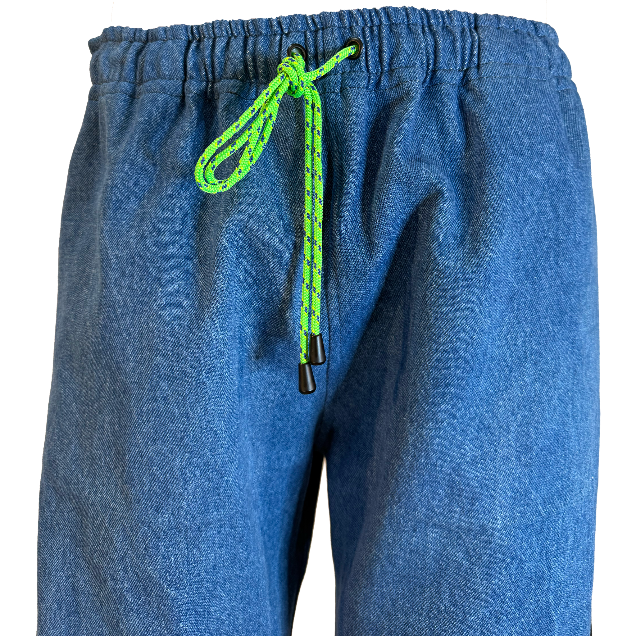 Close-up of blue denim sweatpants with a bright neon green and black patterned drawstring cord tied at the elastic waistband.