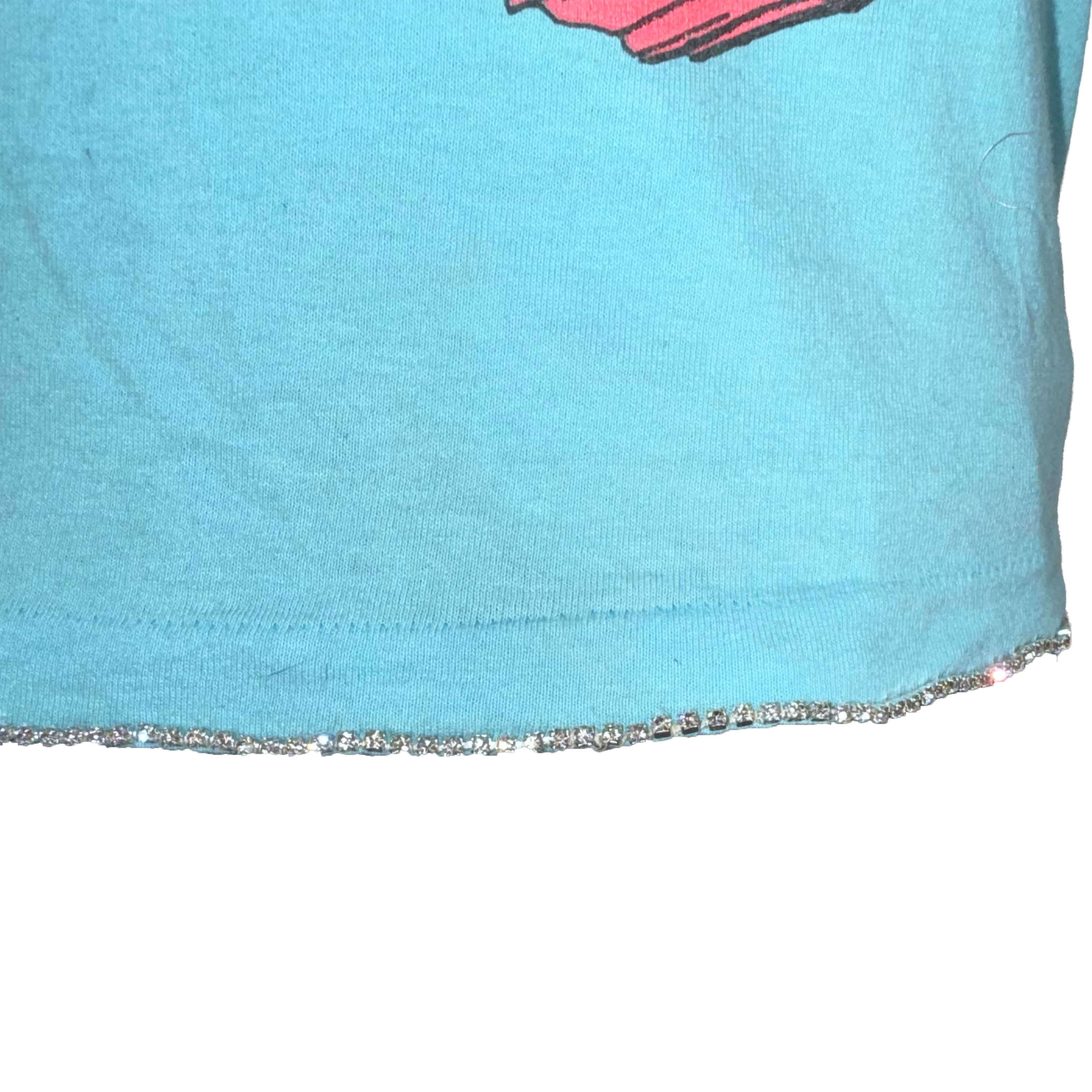 Close-up of a light blue t-shirt hem with a silver rhinestone trim, showing a small portion of a pink graphic print at the top.