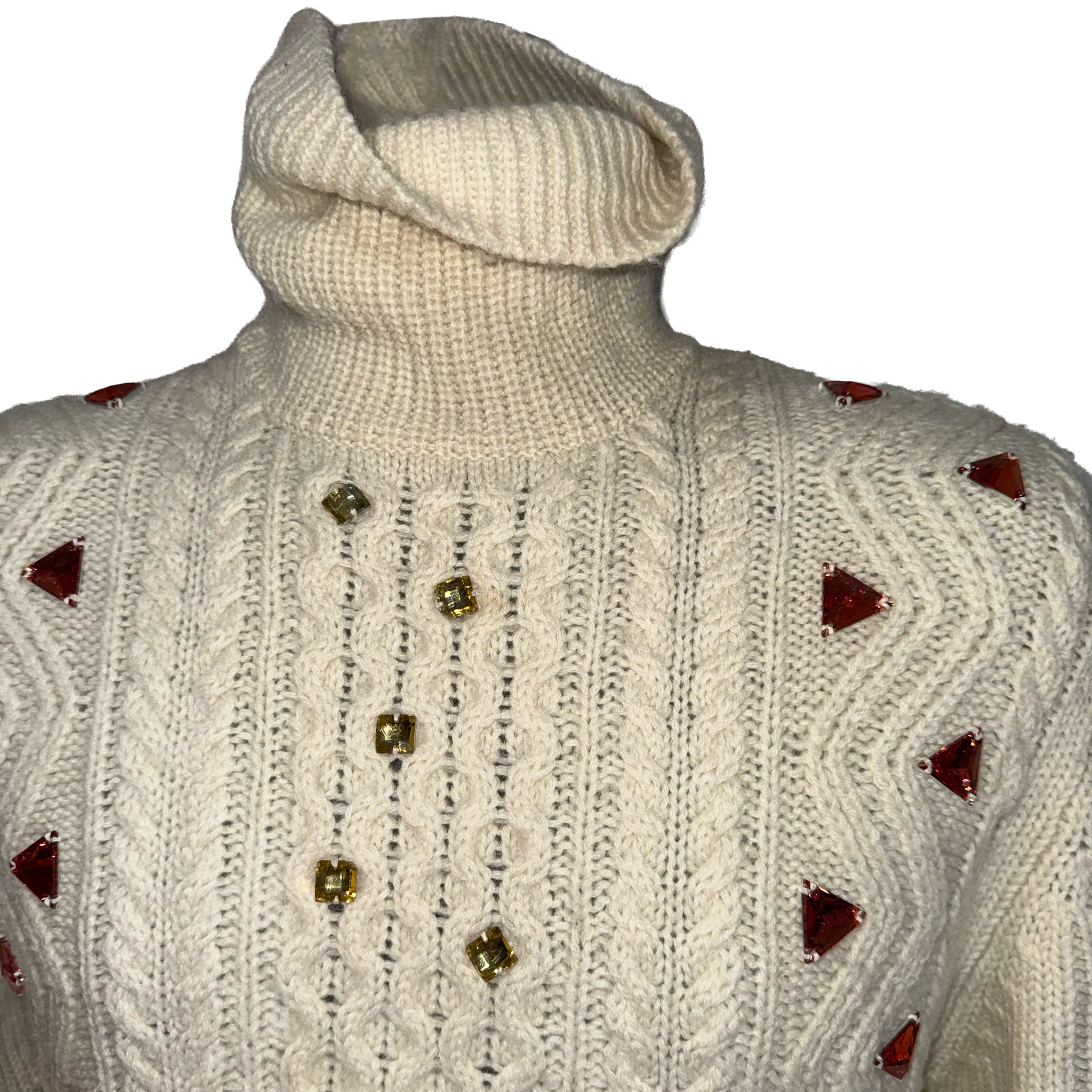 An off-white cable-knit turtleneck sweater with decorative gold and red embellishments, shown against a plain white background.