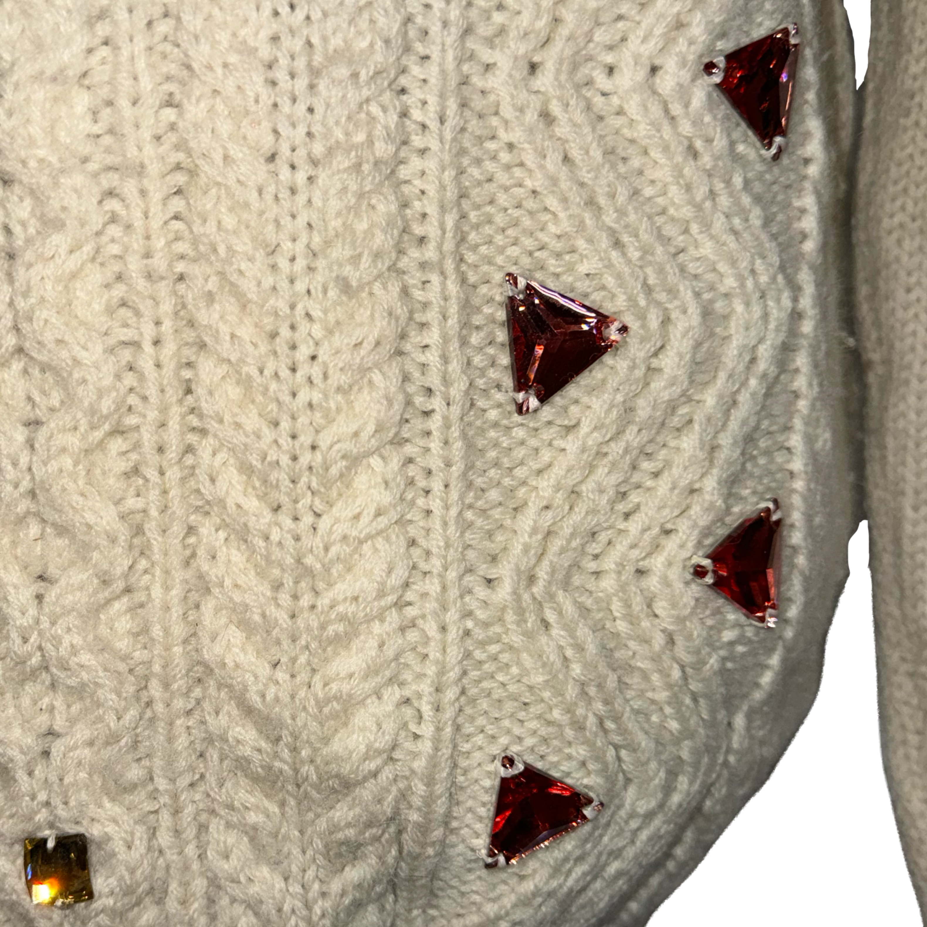 Close-up of a cream cable-knit sweater with red triangular rhinestone embellishments and a few gold square rhinestones on a white background.