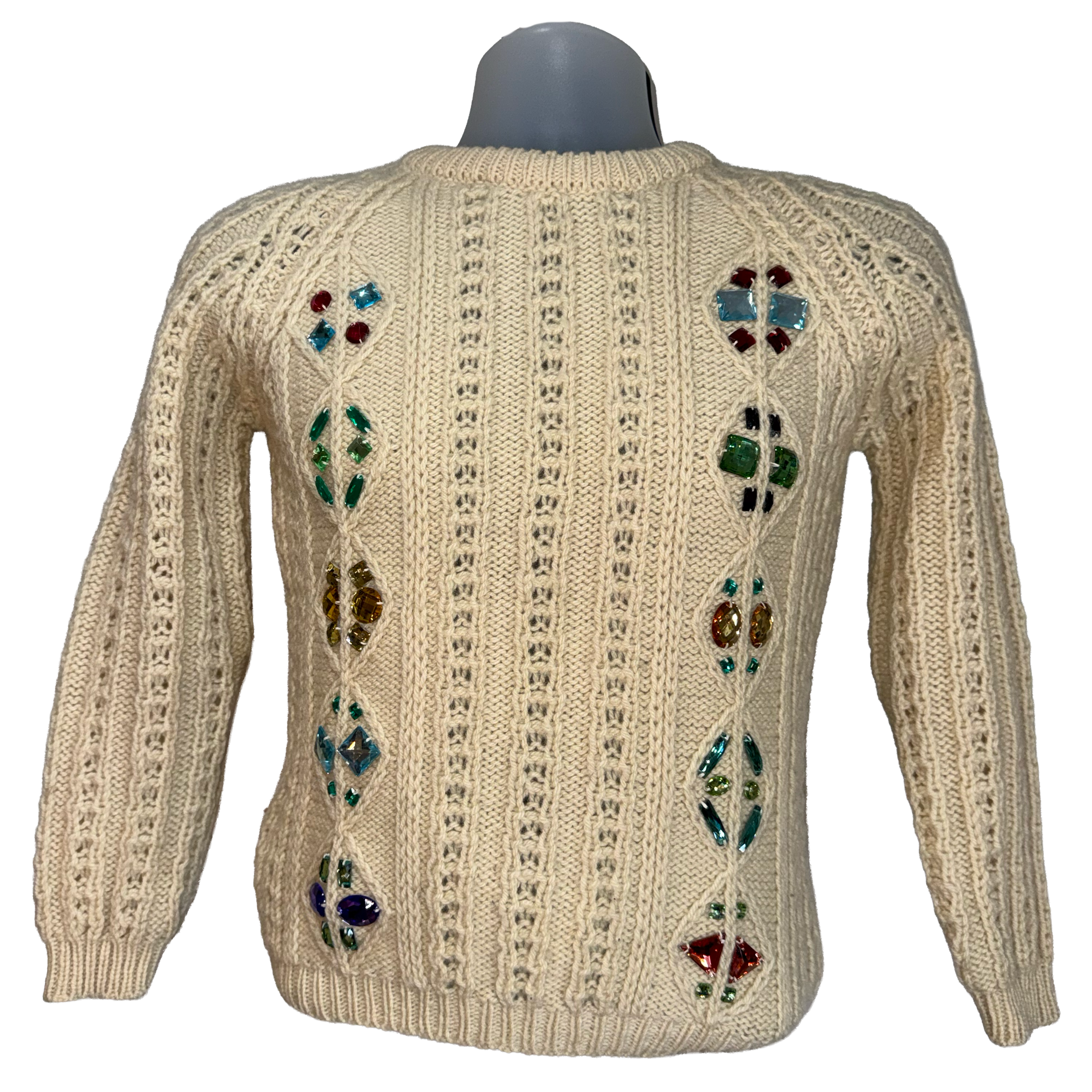 A cream-colored cable-knit sweater displayed on a gray mannequin torso, featuring colorful embroidered floral patterns down the center of the back.