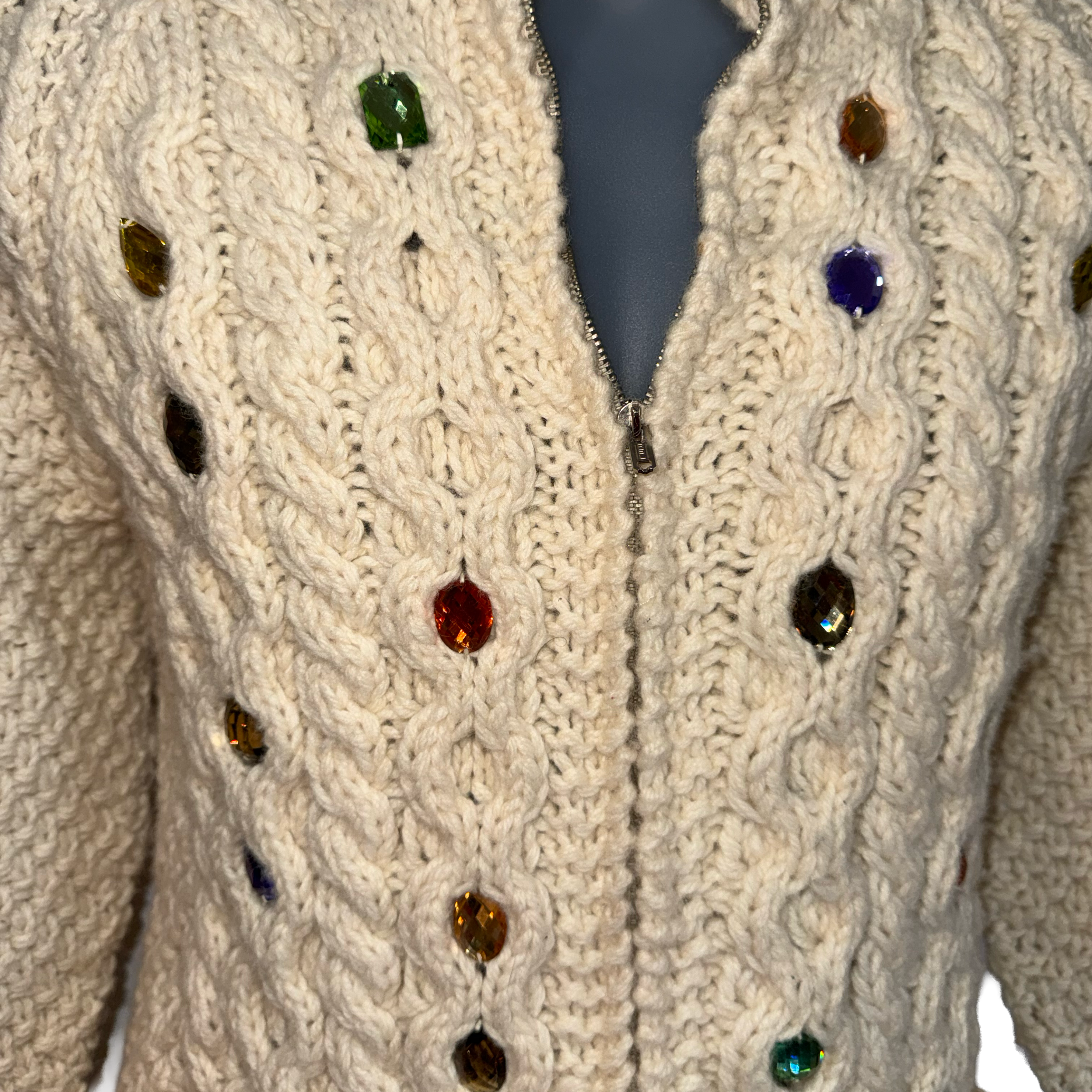 Cream cable-knit zip-up cardigan sweater with colorful faceted gemstone buttons, displayed on a mannequin torso.