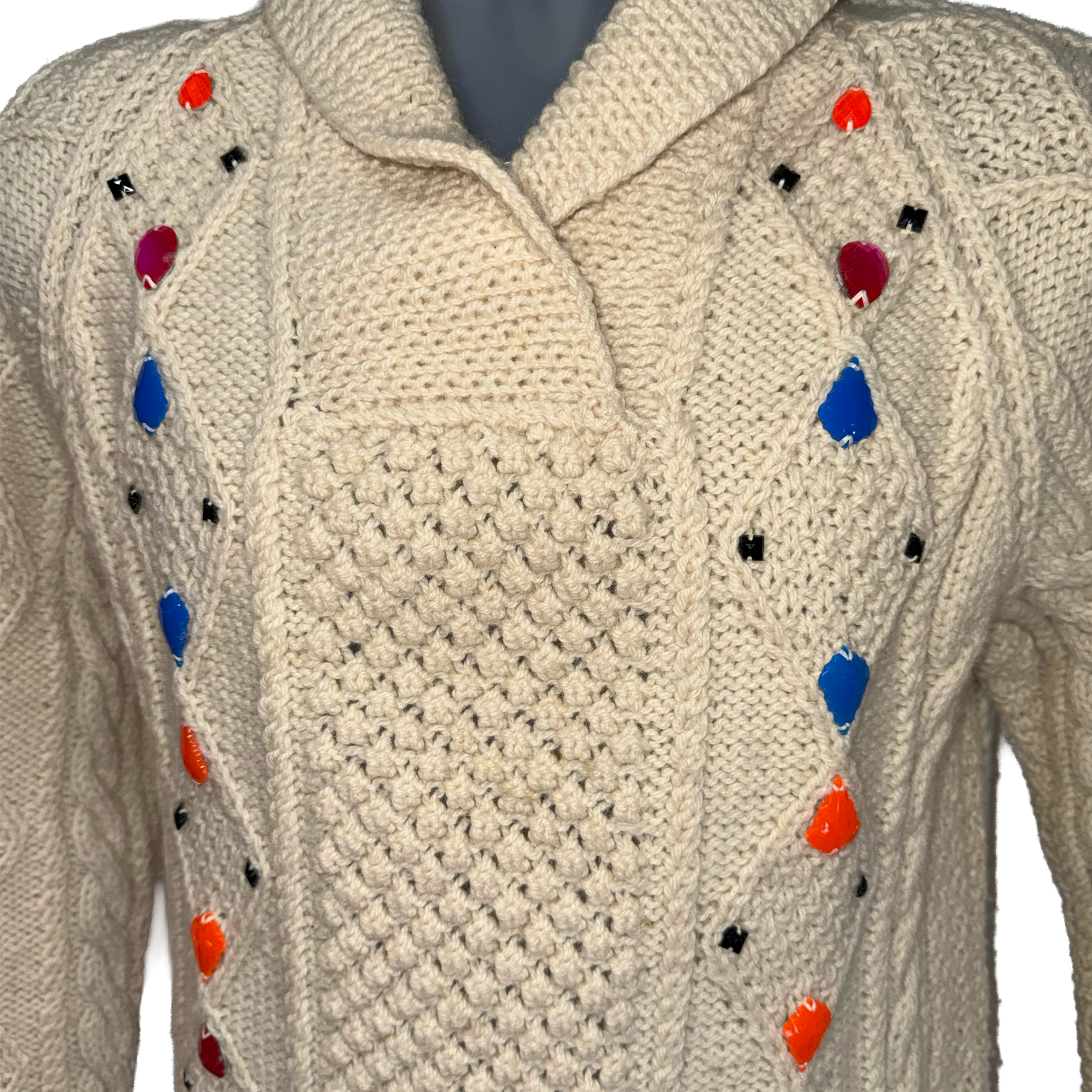 Cream cable-knit sweater with colorful pom-pom accents in blue, red, orange, and black, displayed on a mannequin torso.