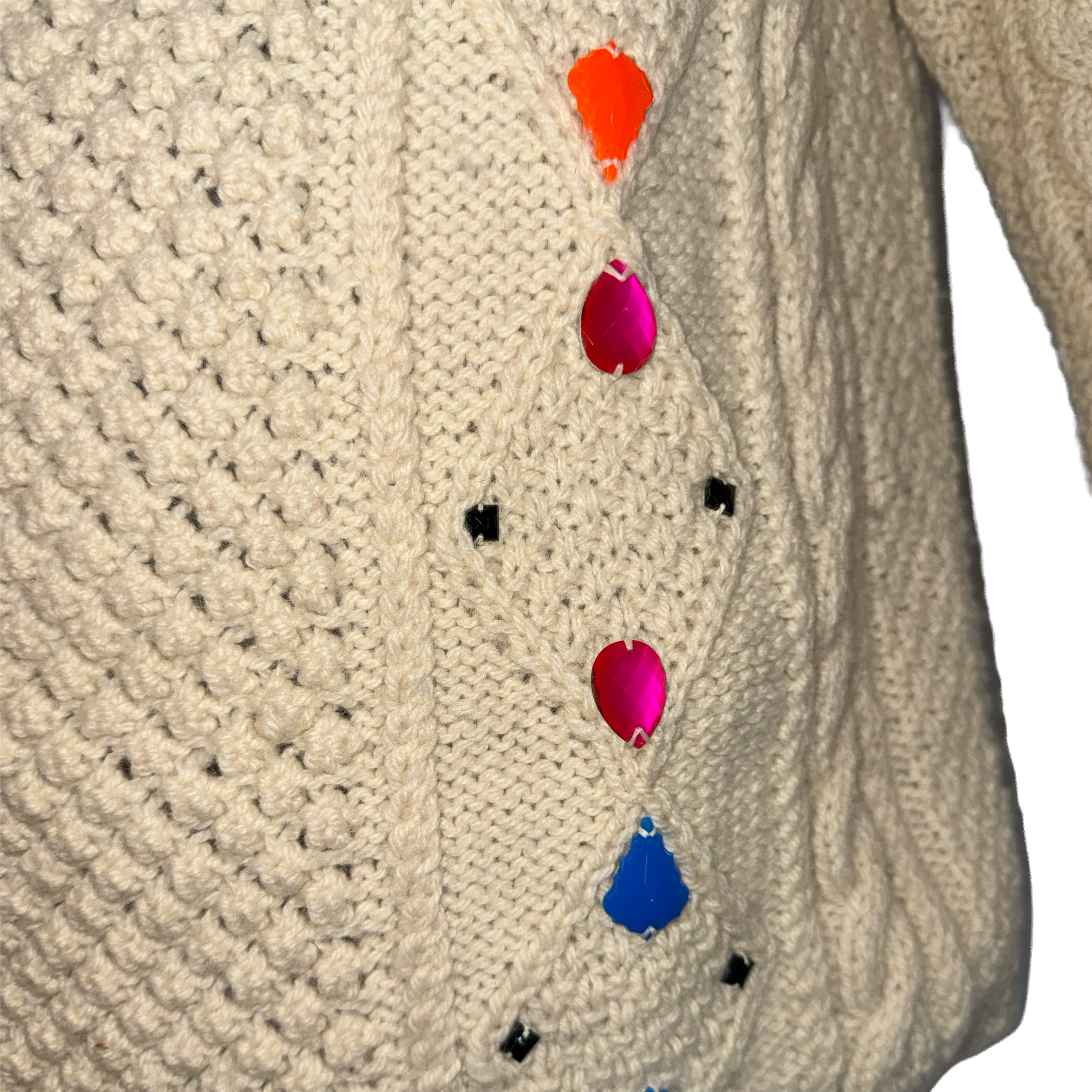 Close-up of a cream-colored cable-knit sweater featuring colorful teardrop-shaped buttons in orange, pink, magenta, blue, and black.