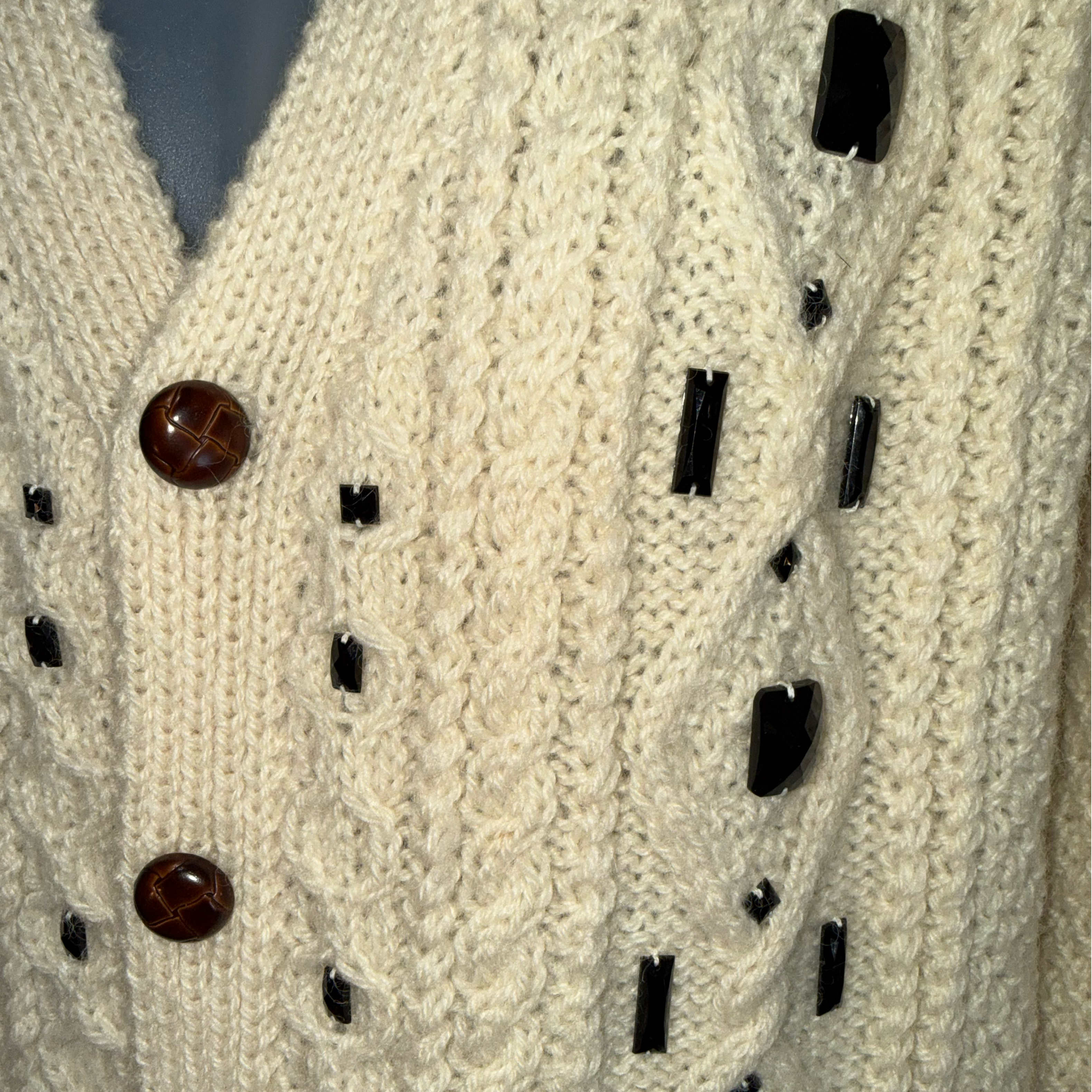 Close-up of a cream cable-knit cardigan sweater with dark brown and black decorative buttons.