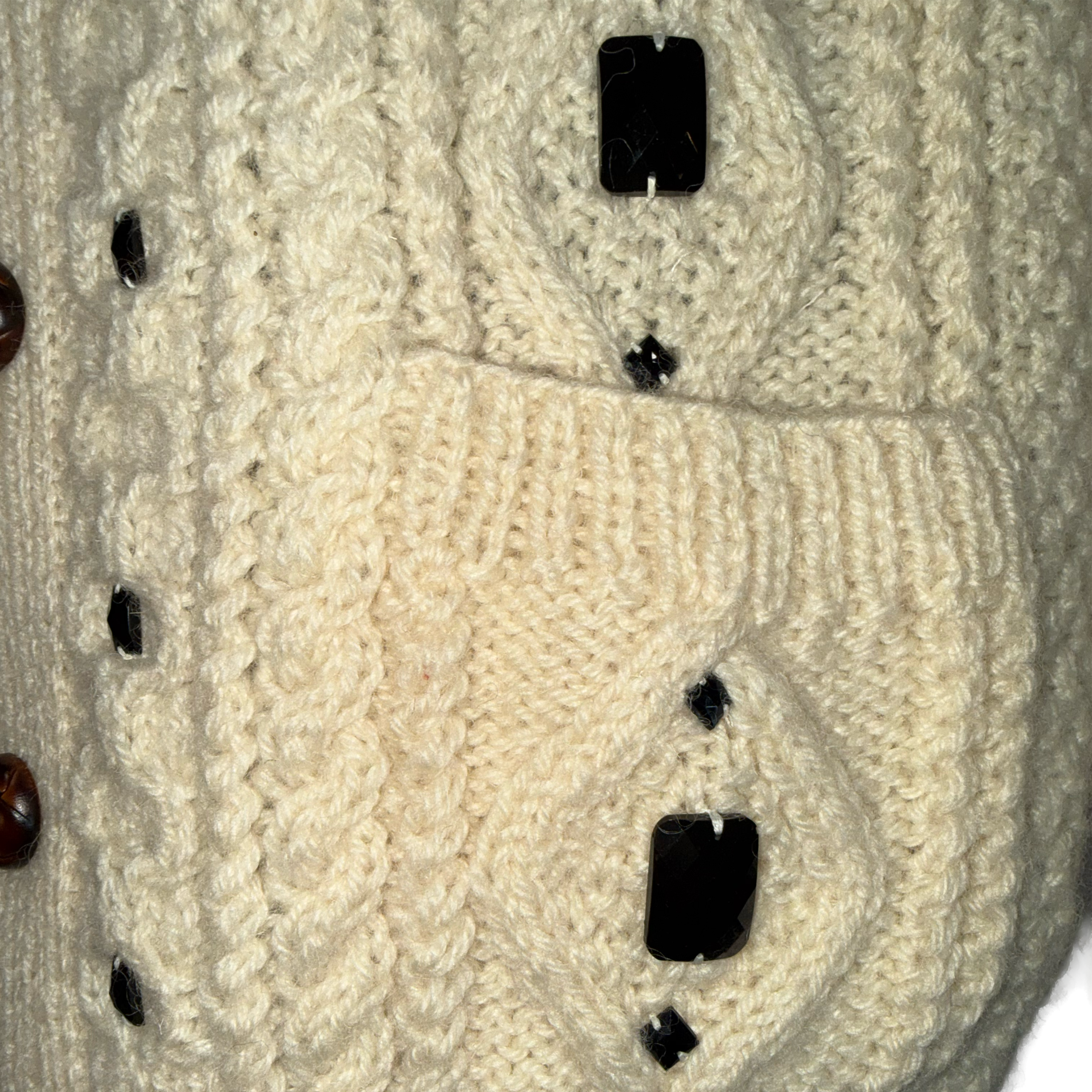 Close-up of a cream cable-knit cardigan sweater with dark brown and black decorative buttons.
