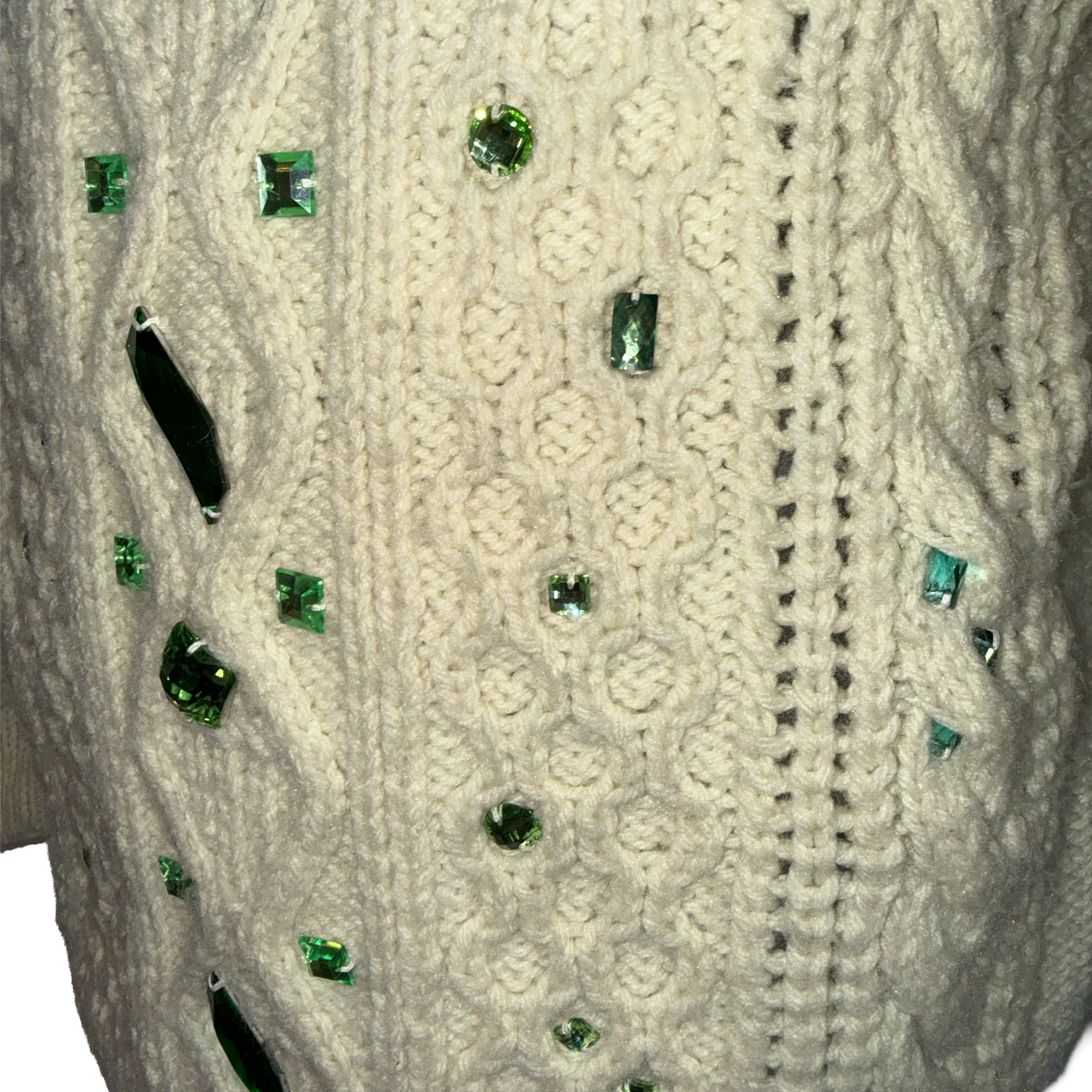 Close-up of a cream cable-knit sweater decorated with scattered green faceted rhinestones.