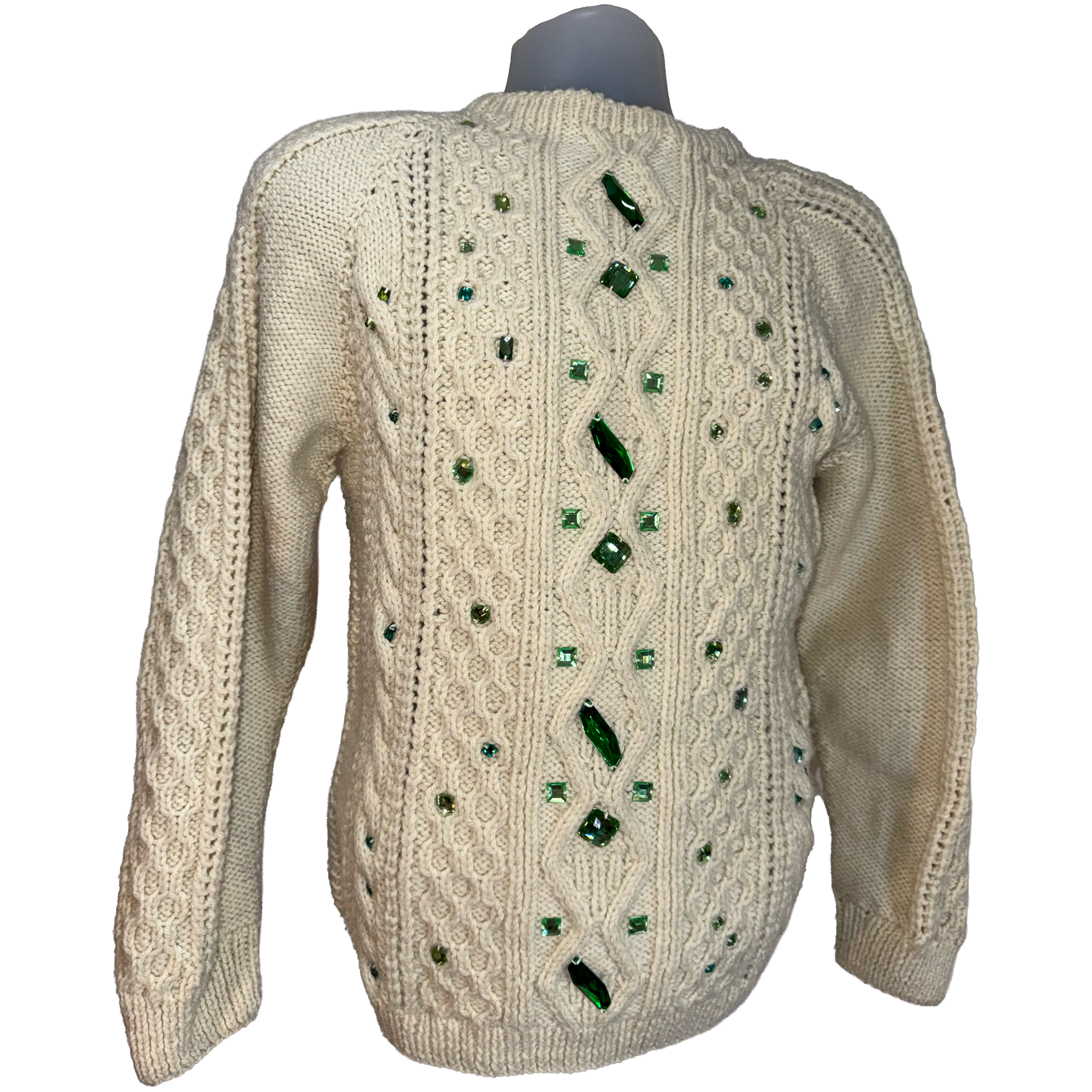 An off-white cable-knit sweater displayed on a mannequin, featuring green faceted rhinestone embellishments arranged vertically down the center back and scattered across the shoulders and sleeves.