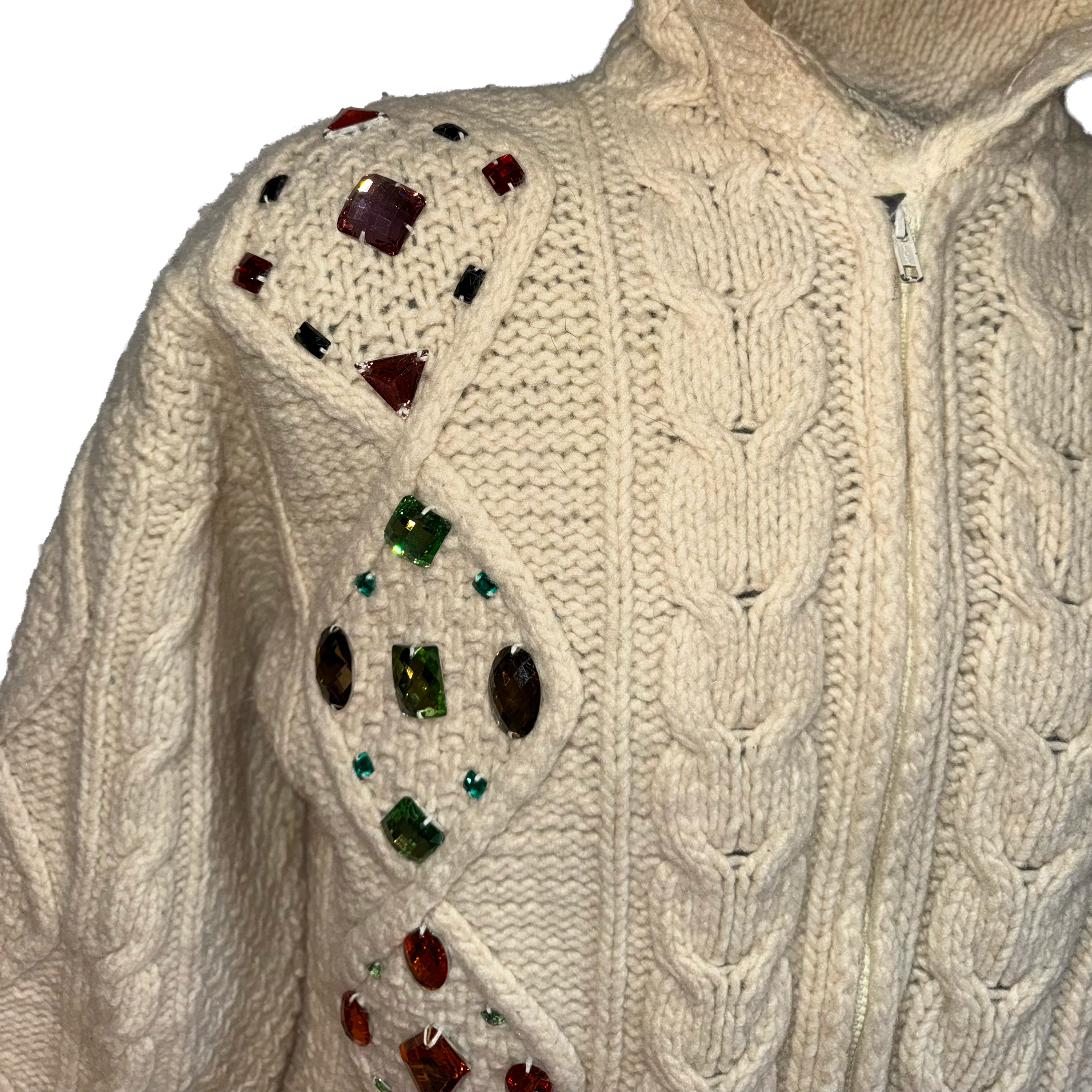 Close-up of a cream cable-knit zip-up sweater with decorative faux jewels embellished on the shoulders and upper chest.