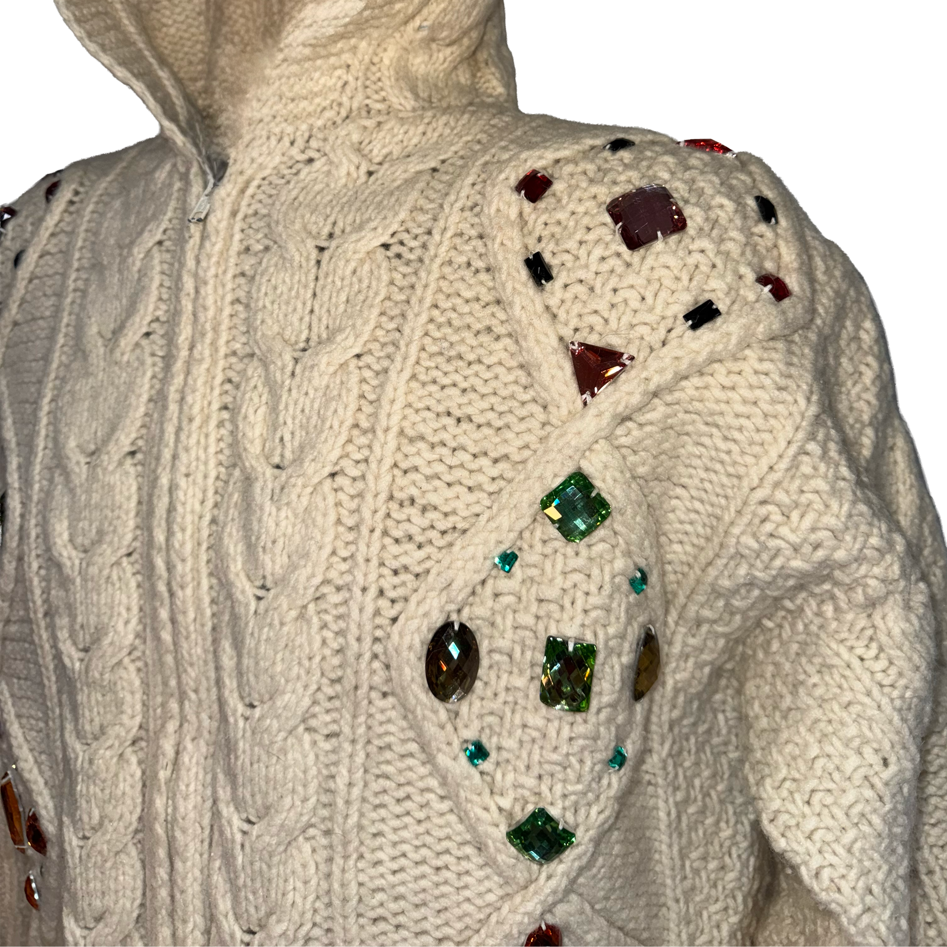 Close-up of a cream cable-knit sweater with decorative multicolored faux gems attached to the shoulders and upper chest, shown against a plain white background.