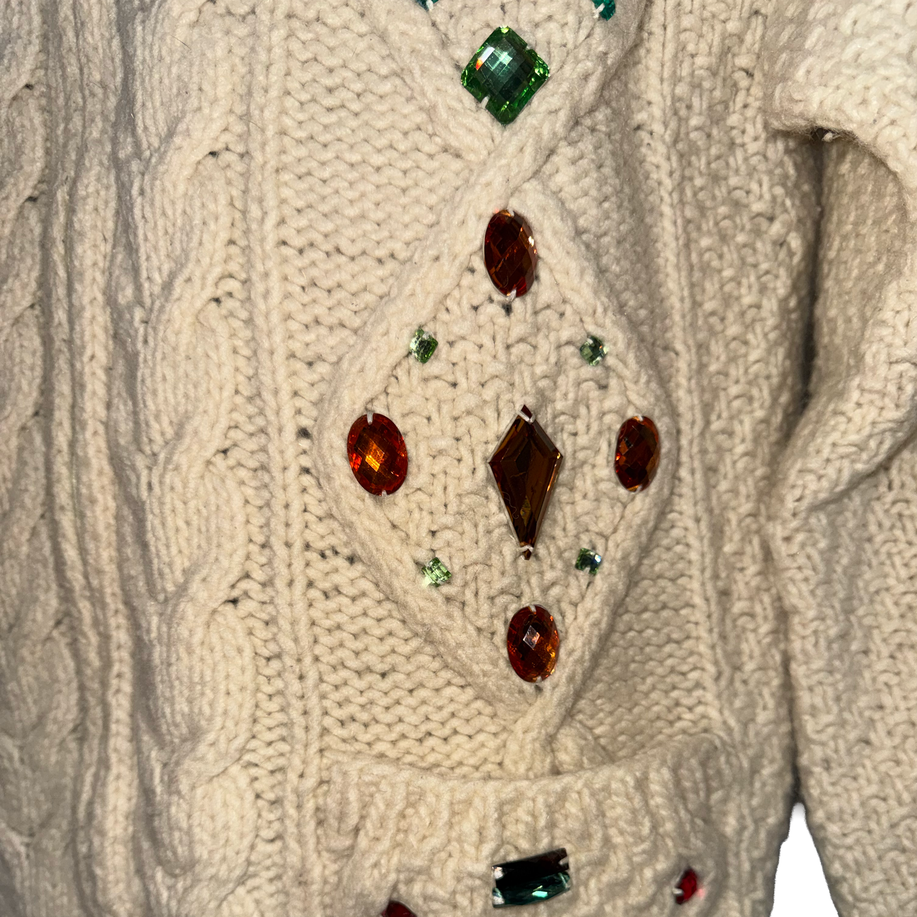 Close-up of a cream cable-knit sweater decorated with faux gemstones in a diamond pattern on the chest.