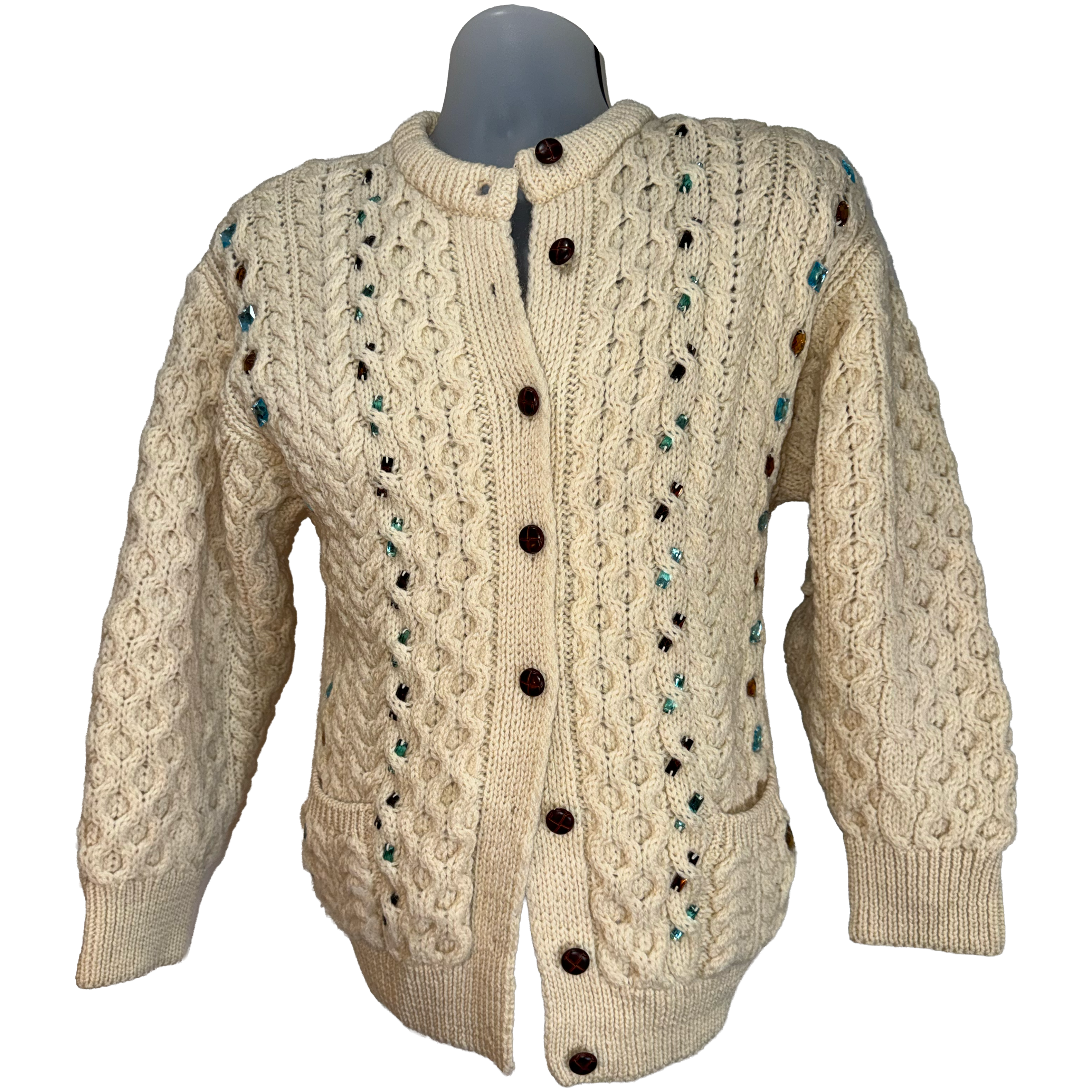 Cream cable-knit cardigan sweater with dark brown buttons and small teal and black yarn accents, displayed on a gray mannequin torso against a white background.